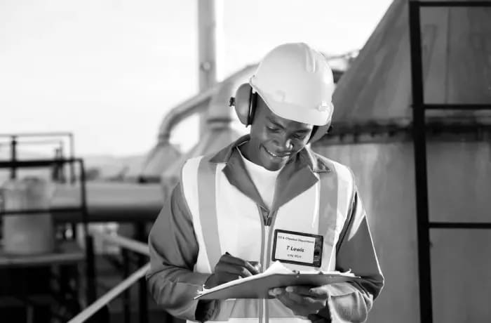 Site worker in a hard hat and hi-vis vest checking a clipboard at an industrial plant